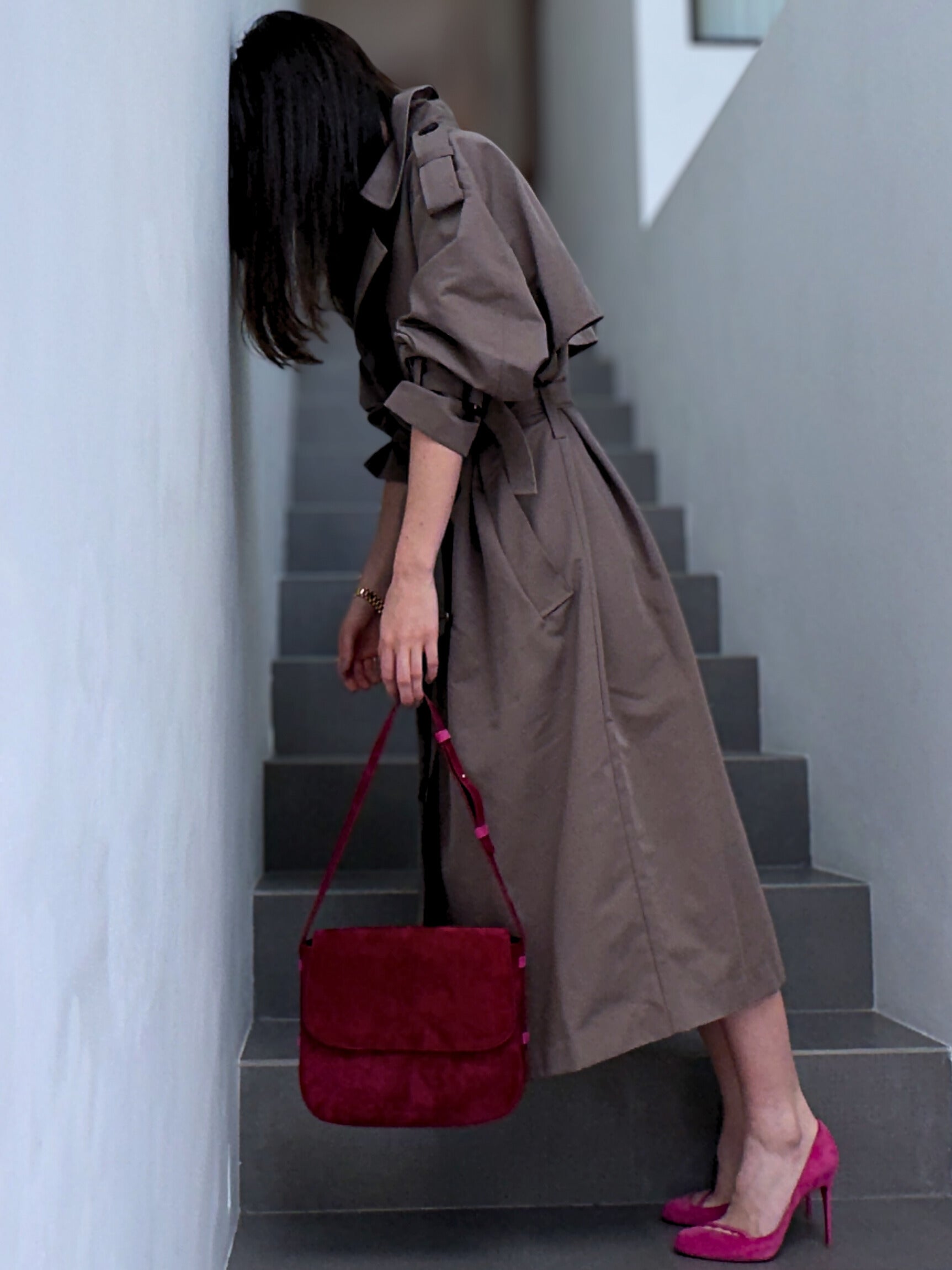 Woman in a trench coat holding a red handbag on a staircase