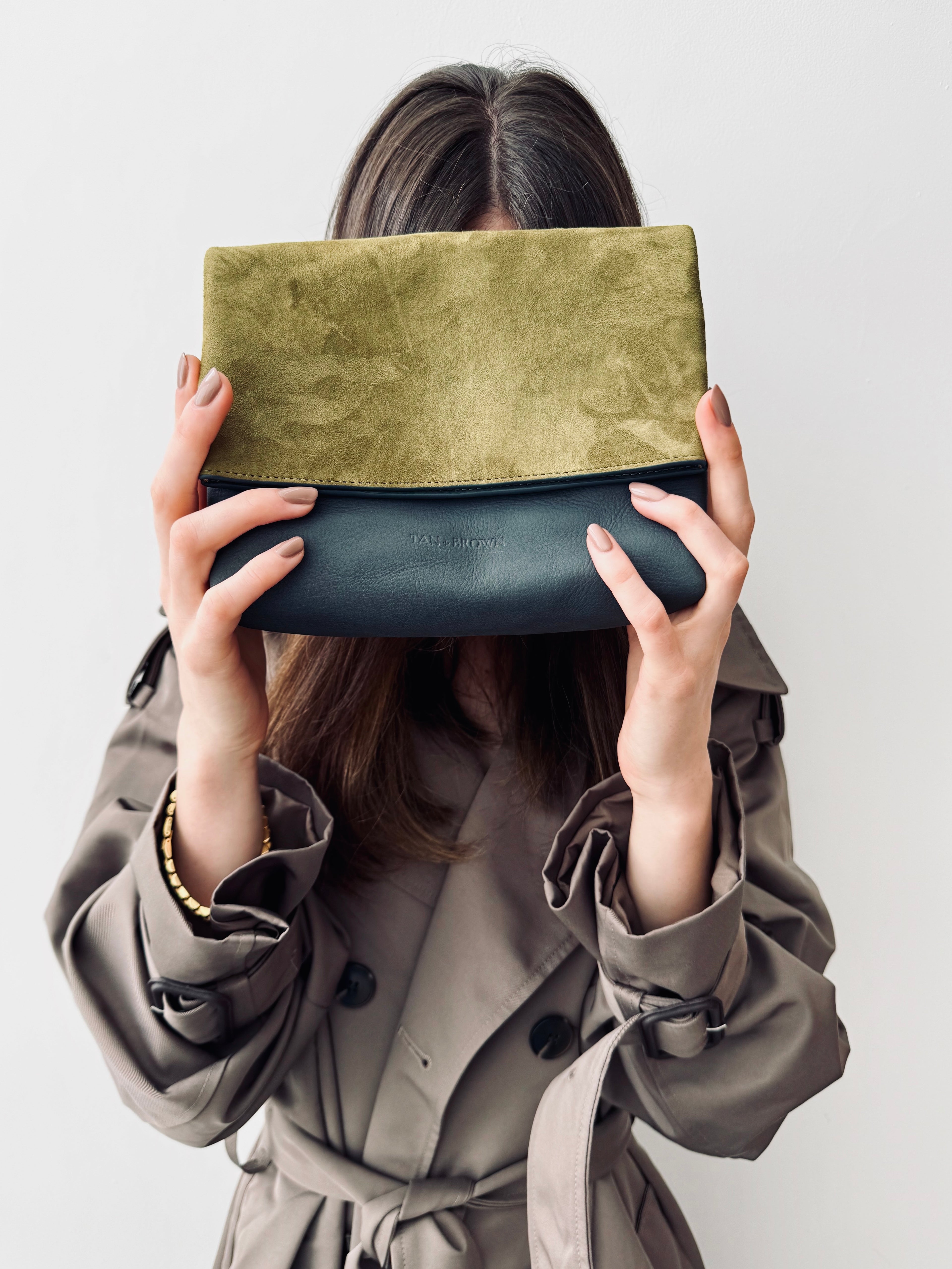Person holding a green and black clutch bag against a plain background