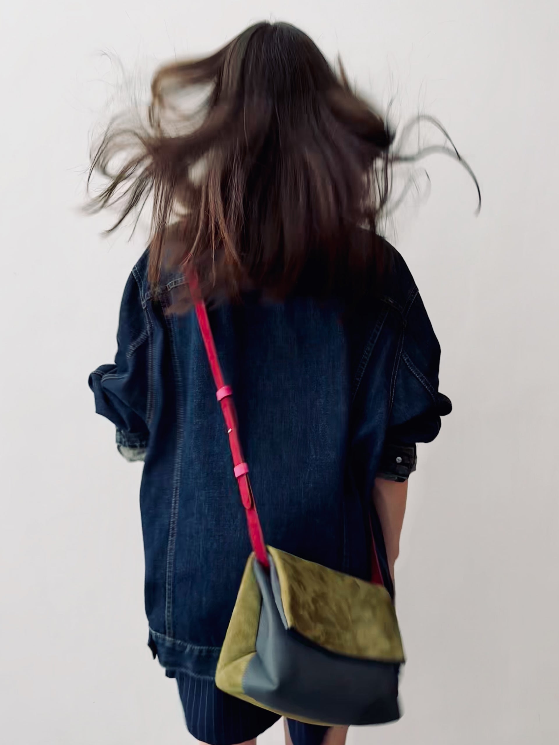 Person wearing a denim jacket with a colorful shoulder bag on a plain background