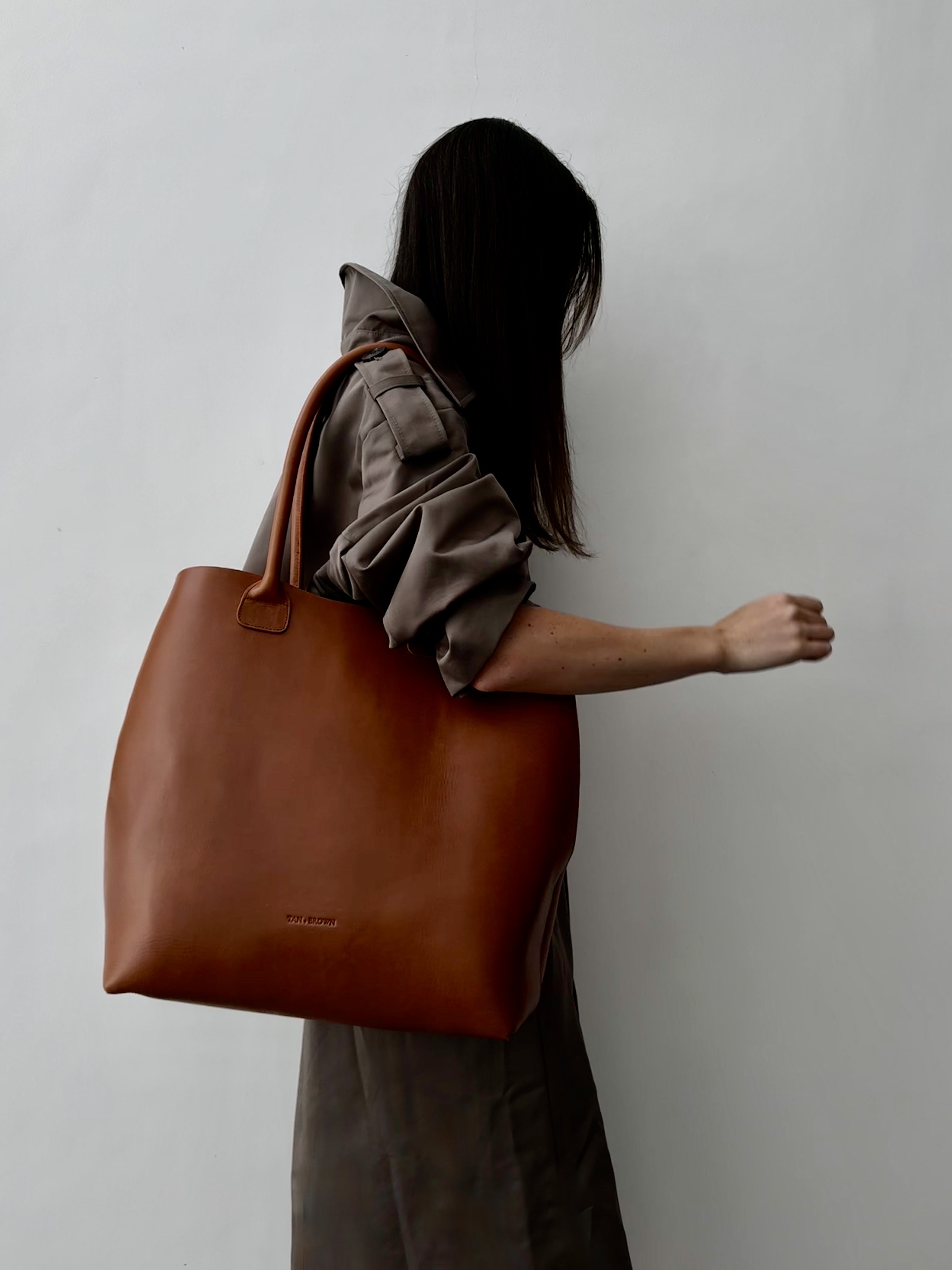 Person holding a brown leather tote bag against a plain background