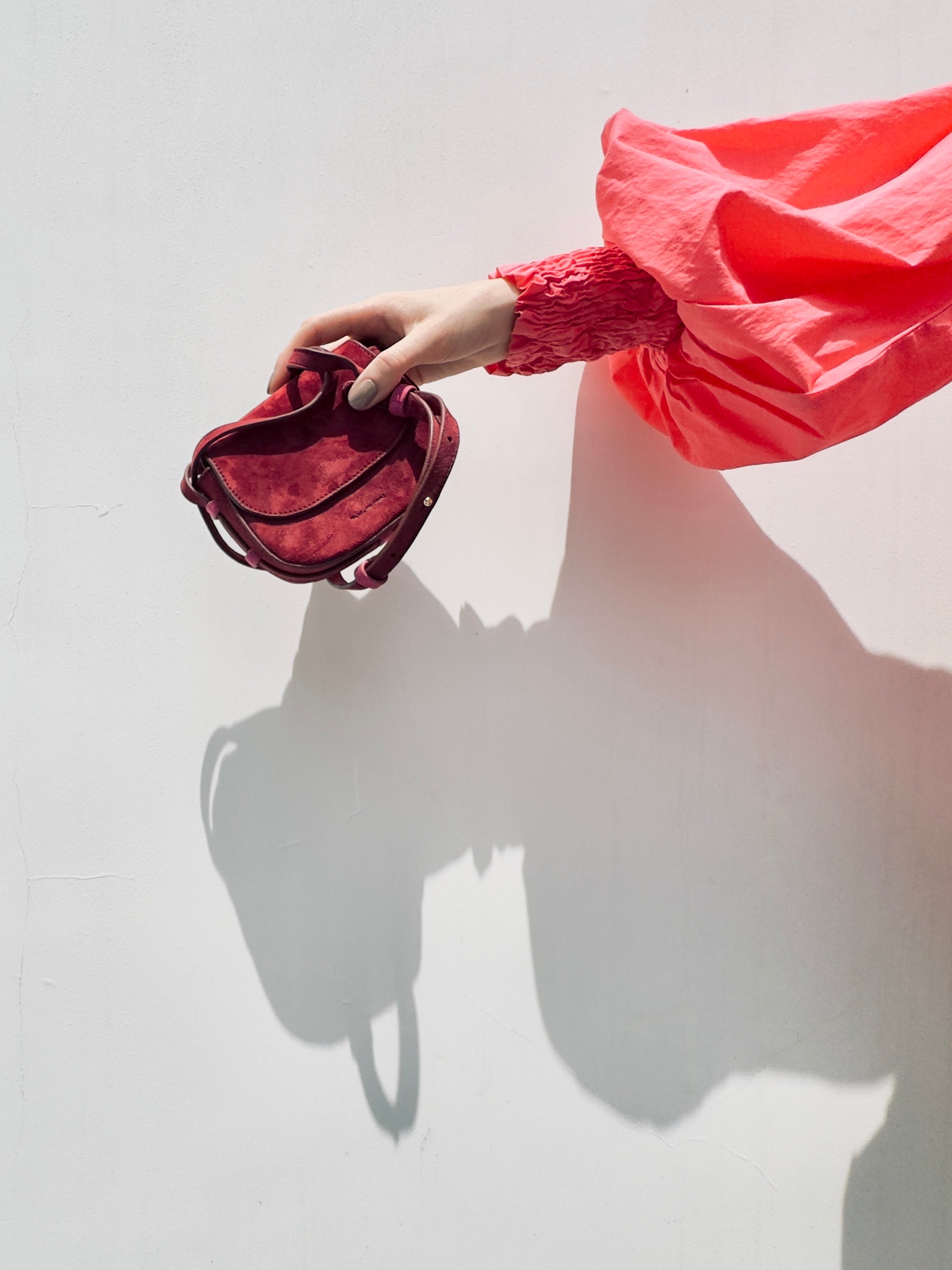 Hand holding a red handbag against a white background