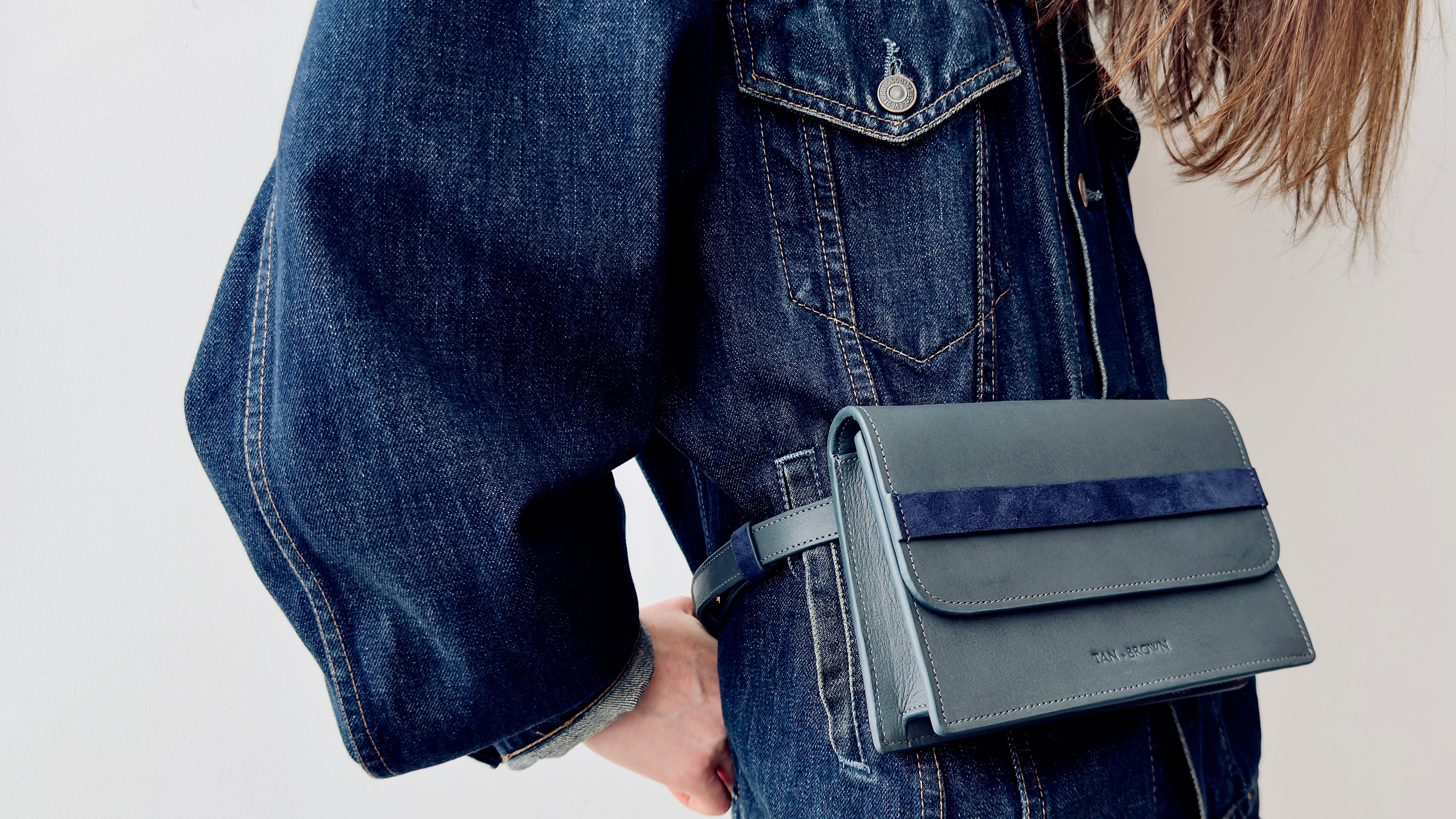 Person holding a blue handbag with a visible brand logo against a neutral background wearing a denim jacket.