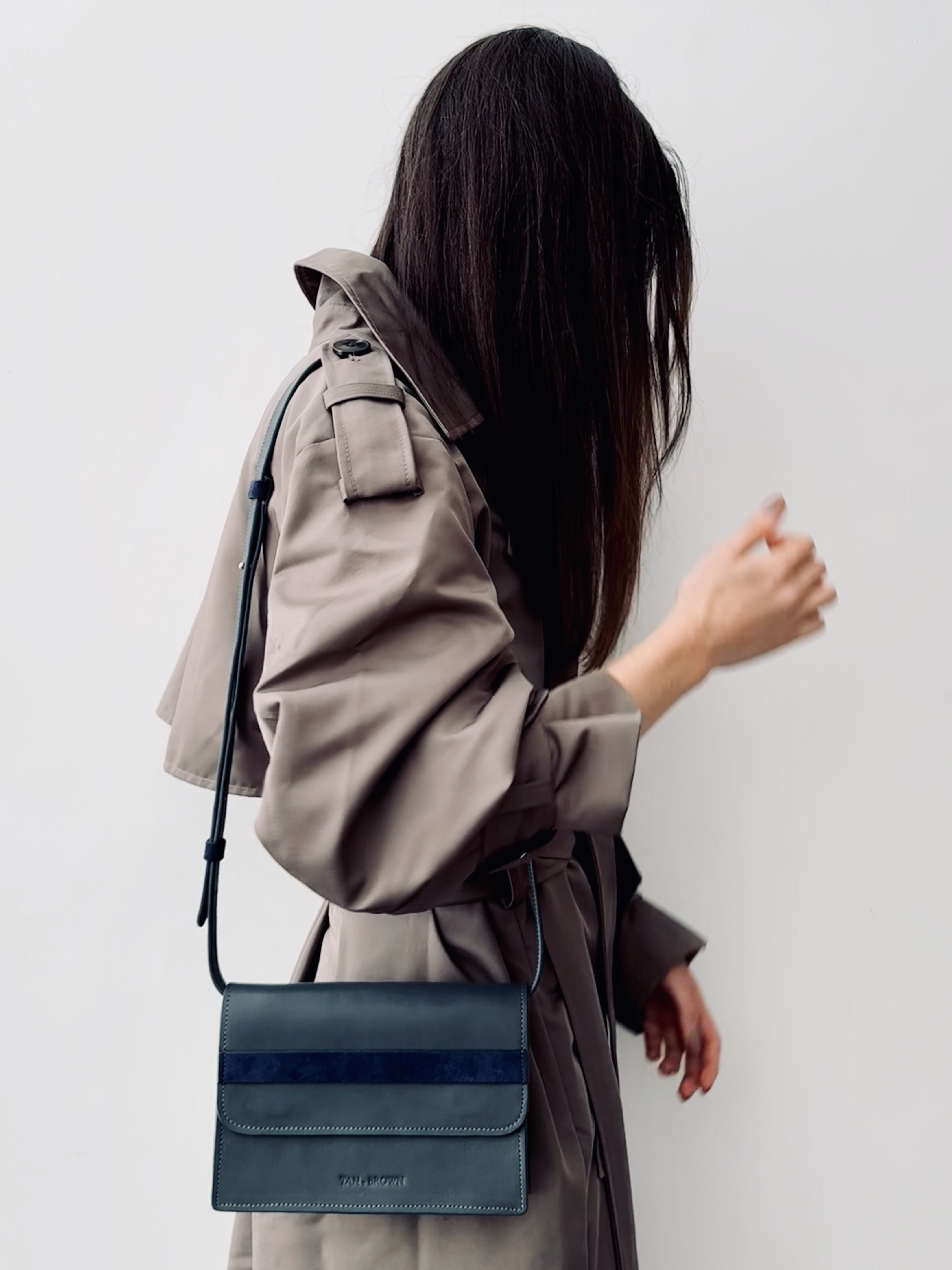 Person wearing a trench coat with a blue handbag on a plain background