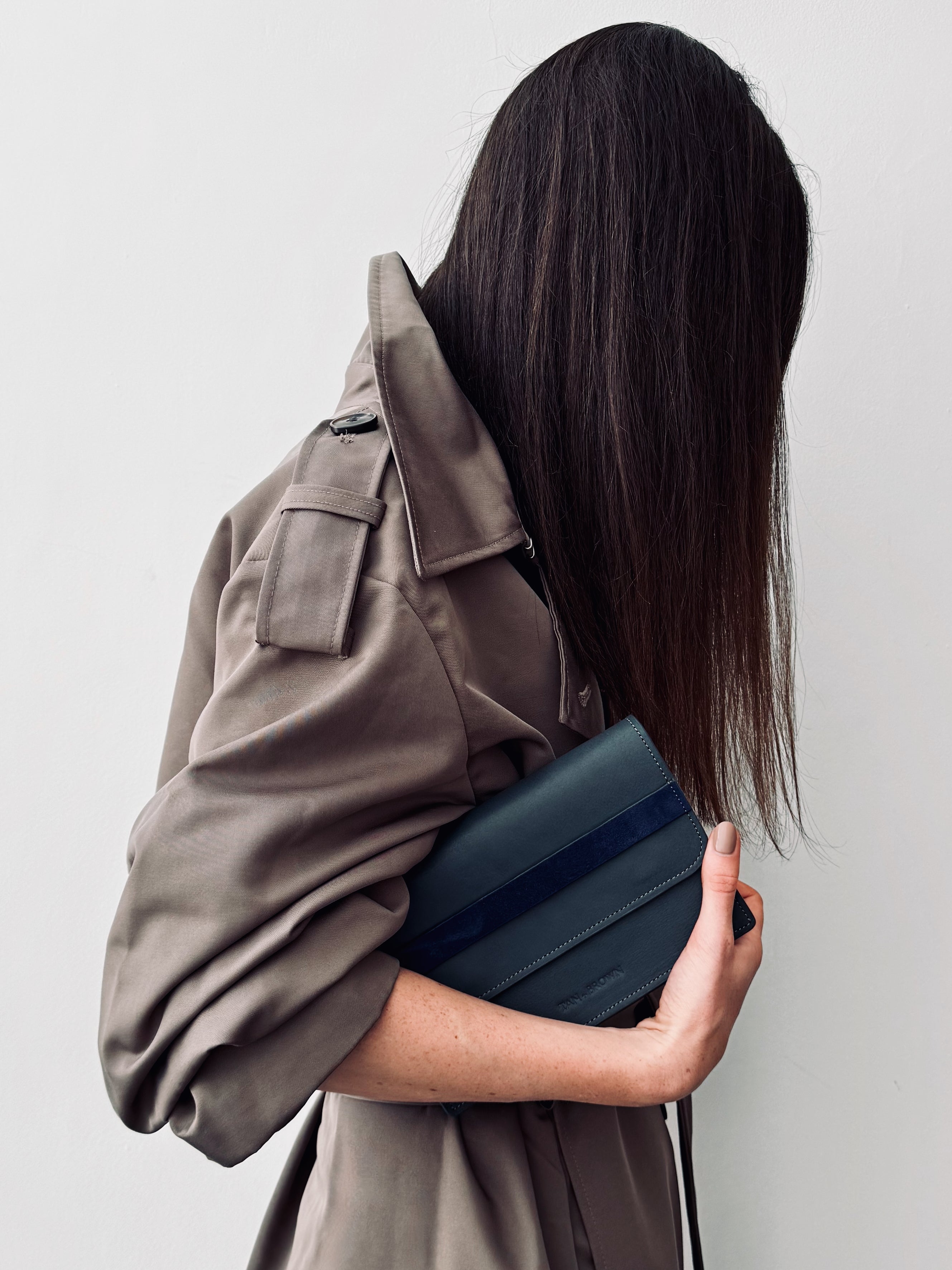 Person holding a dark blue rectangular clutch against a plain background