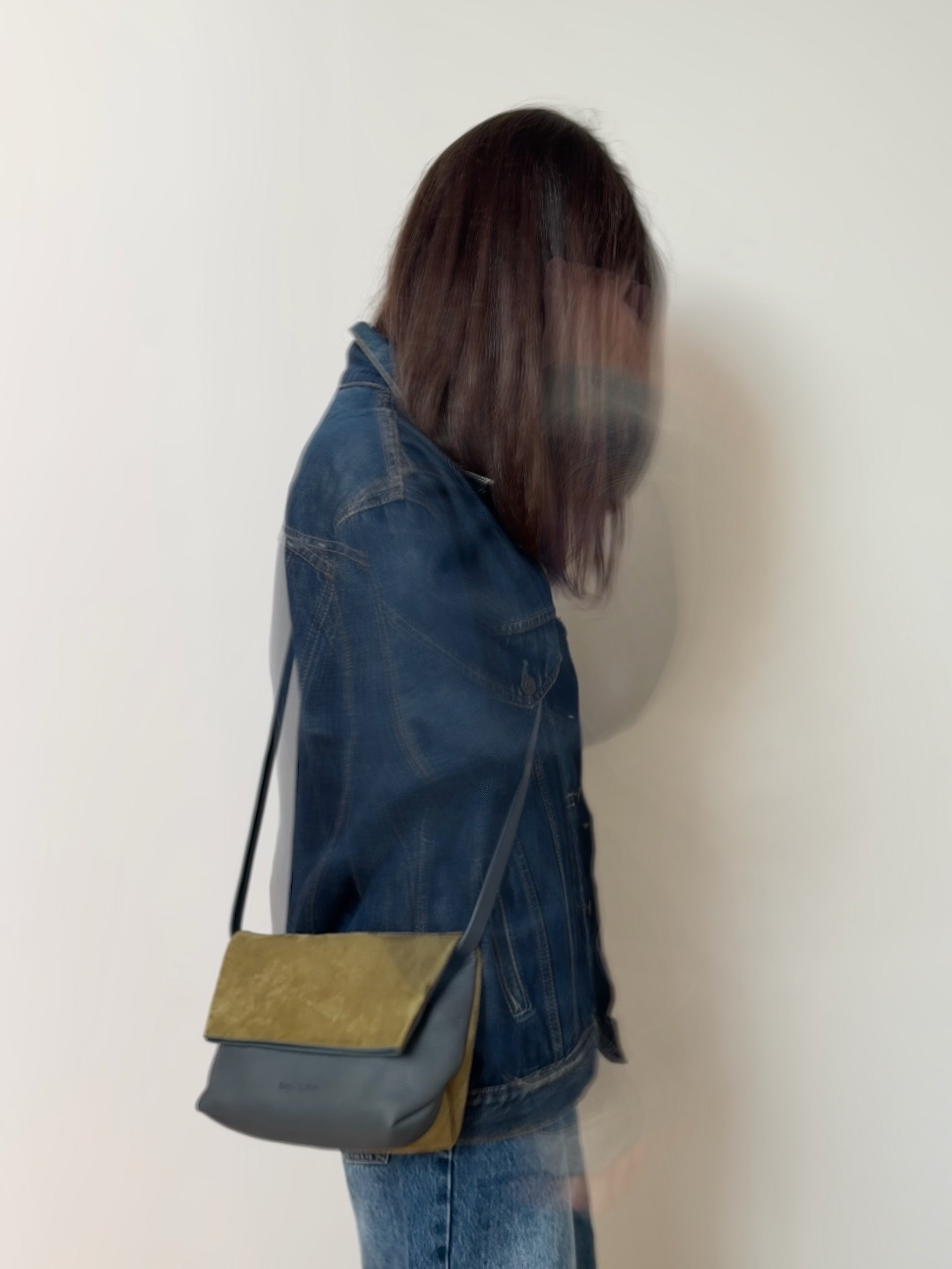 Person wearing a denim jacket with a green crossbody bag against a white background