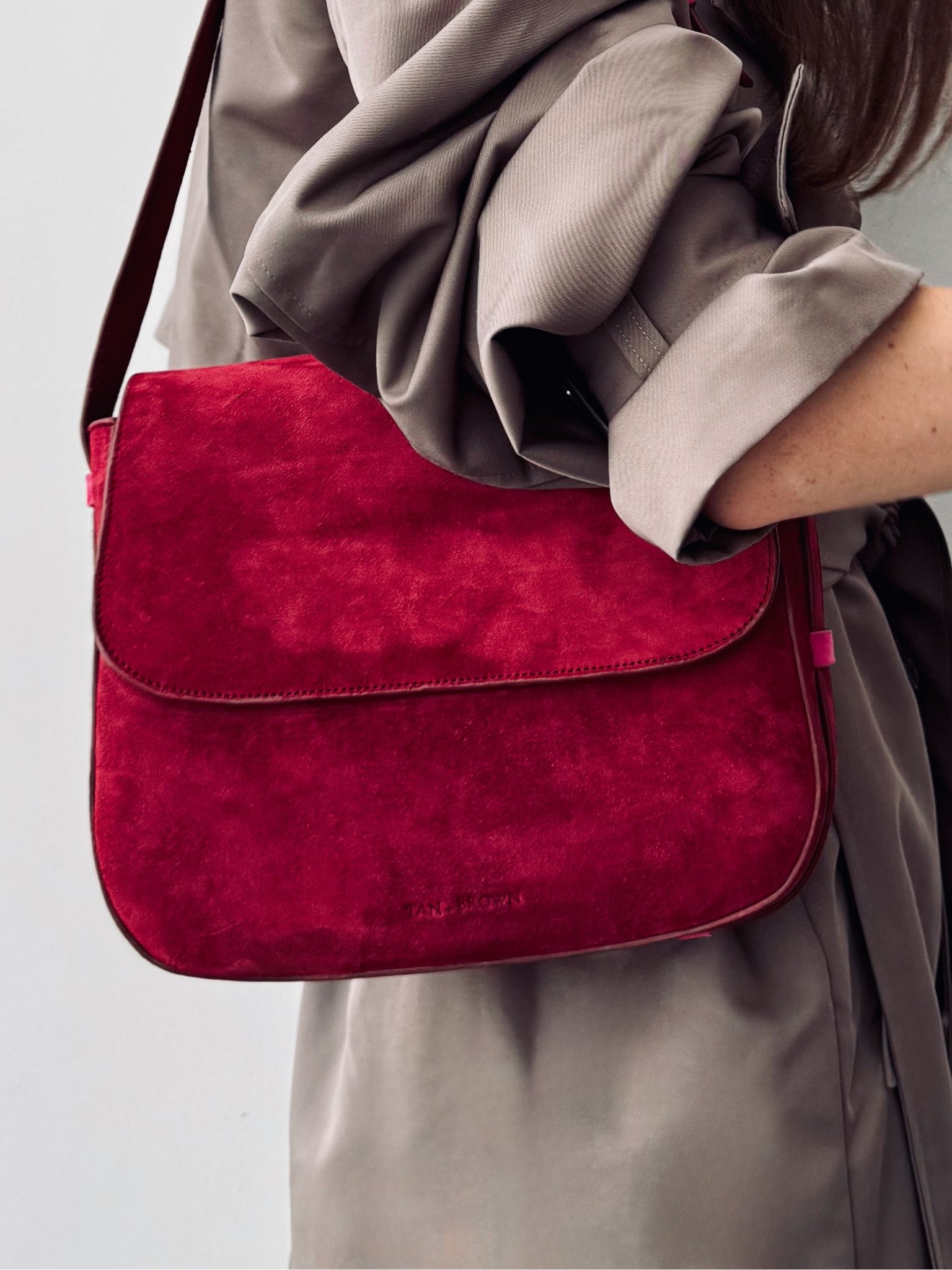 Red handbag held by a person wearing a beige coat on a light gray background
