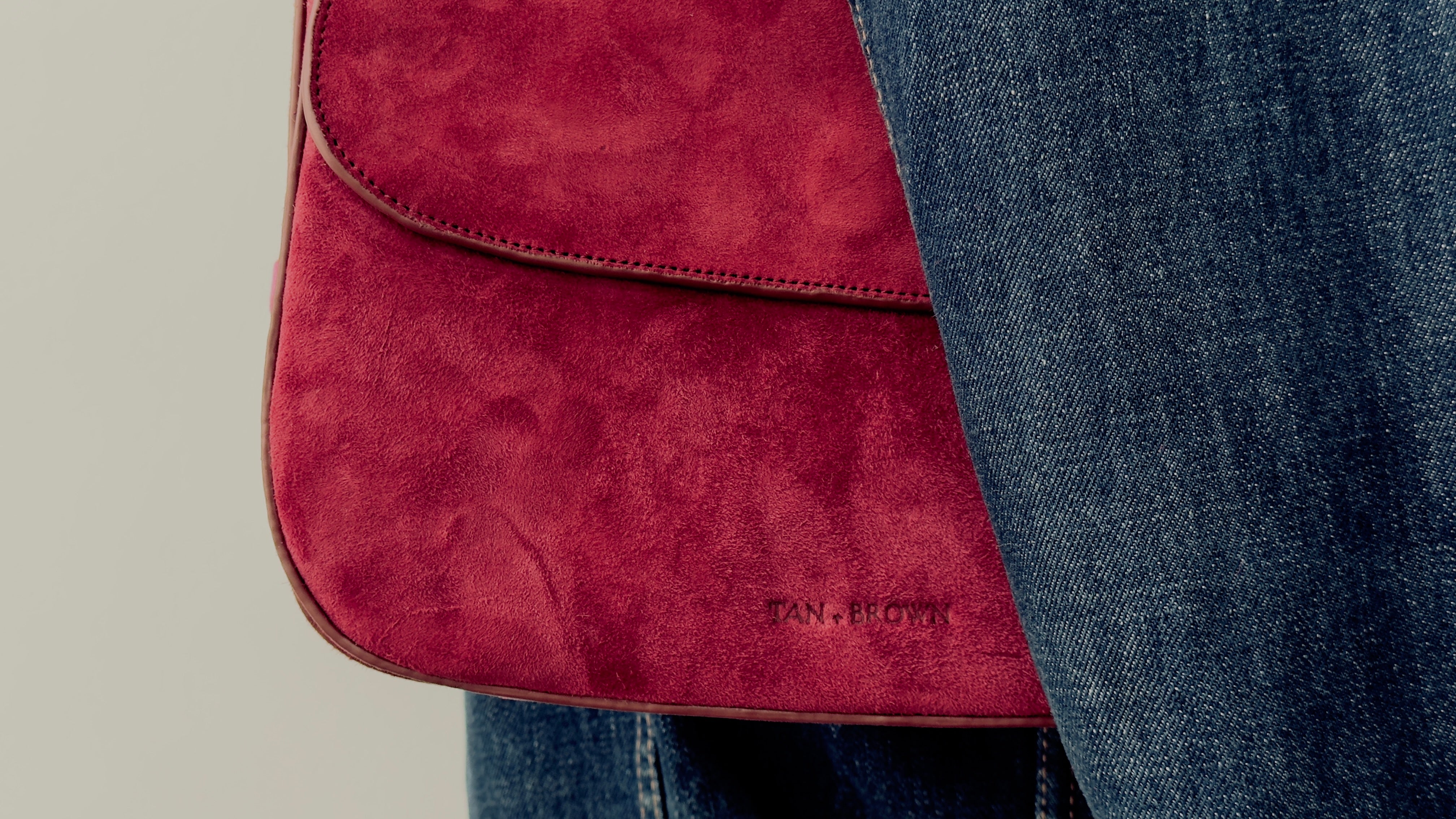 Red handbag held by a person wearing blue jeans on a neutral background