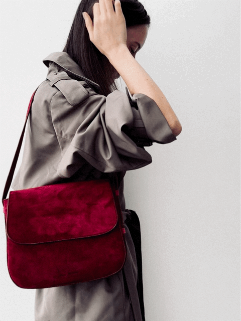 Woman in grey trench coat wearing a large red shoulder bag with a white background
